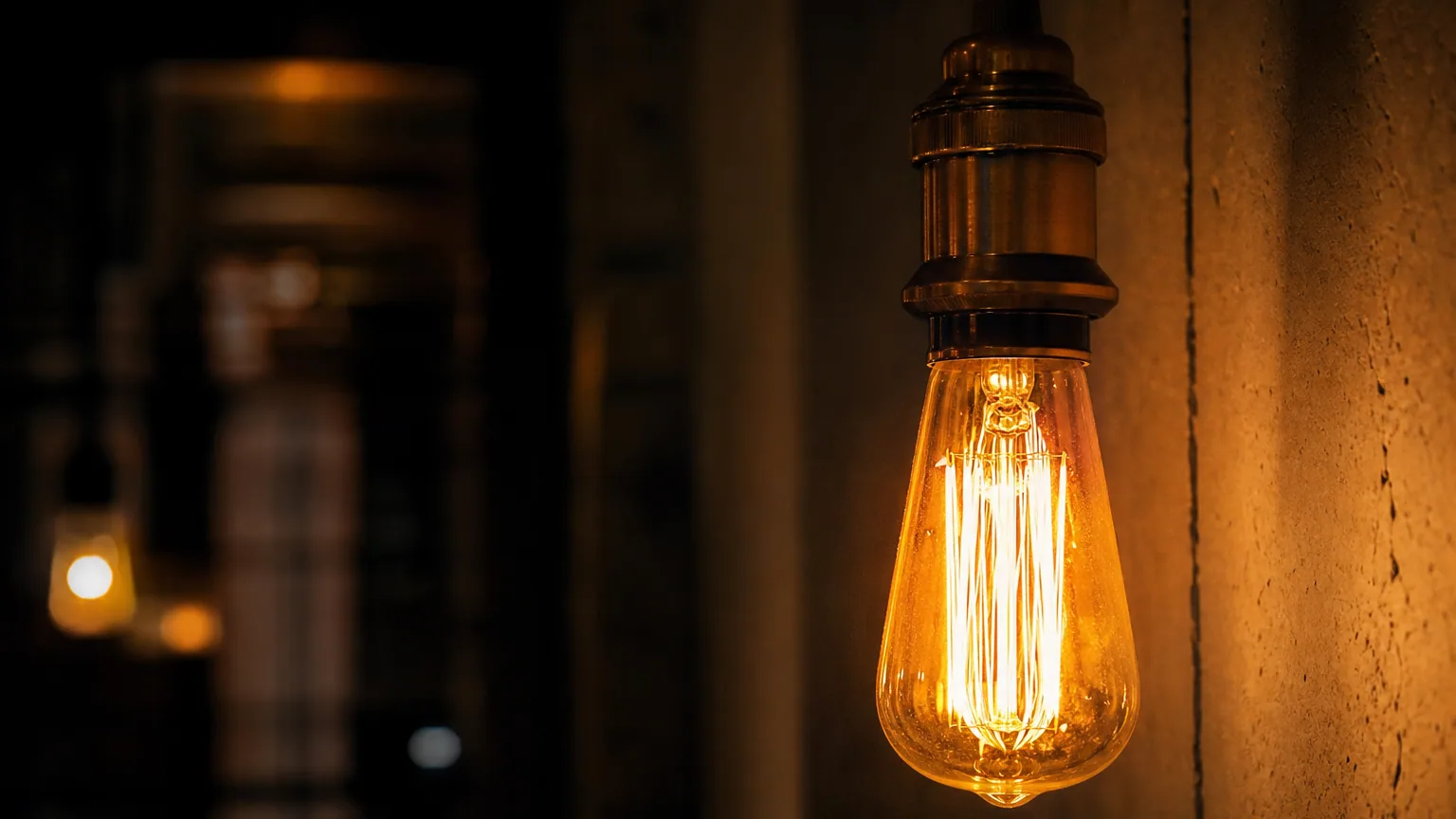 Ampoule à filament allumée dans une douille apparente, gros plan sur le filament incandescent, lumière chaude dans une pièce sombre.