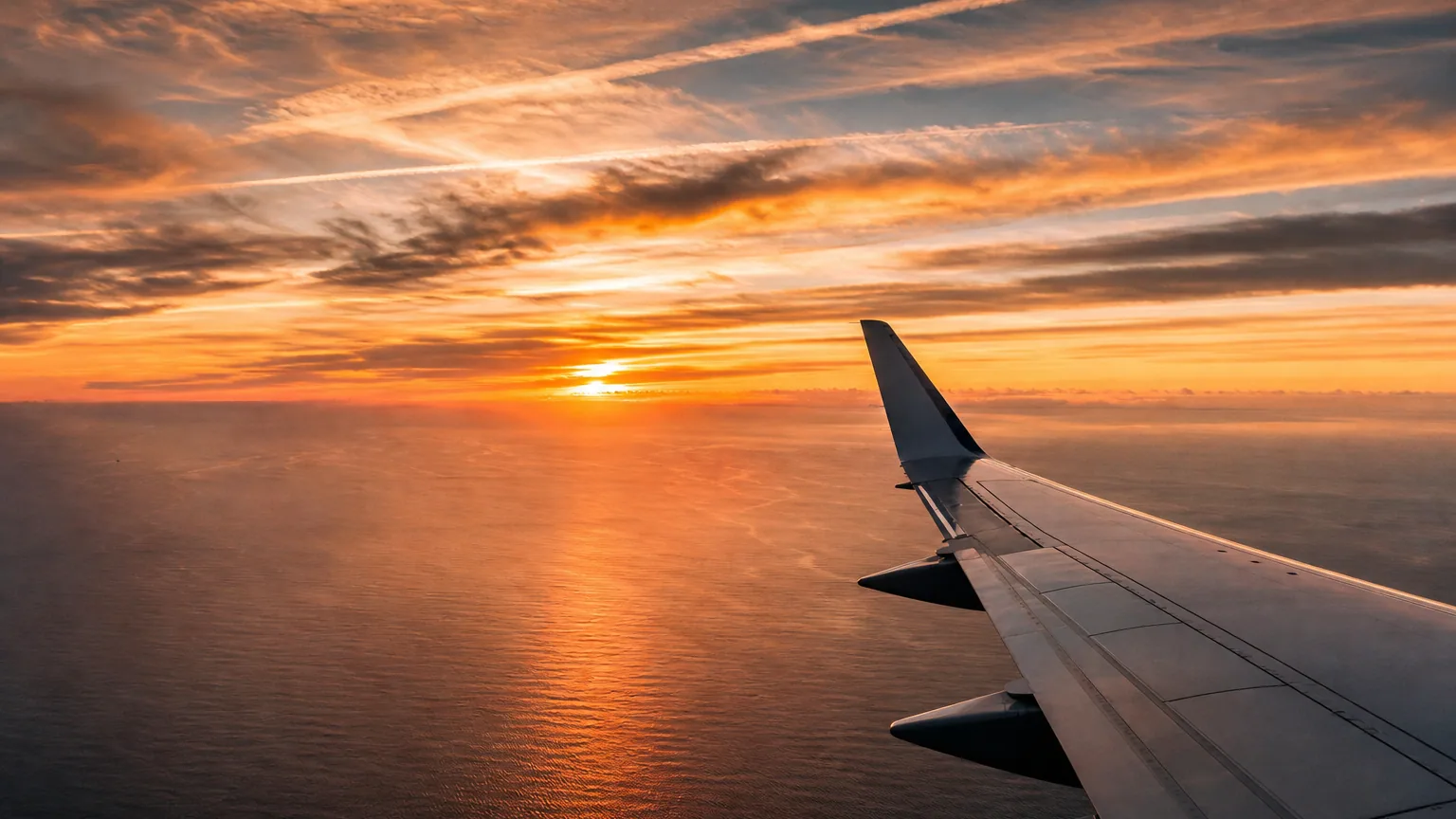 Avion de ligne survolant l'océan Atlantique au coucher du soleil, longues traînées de nuages étirées par le vent d'altitude.