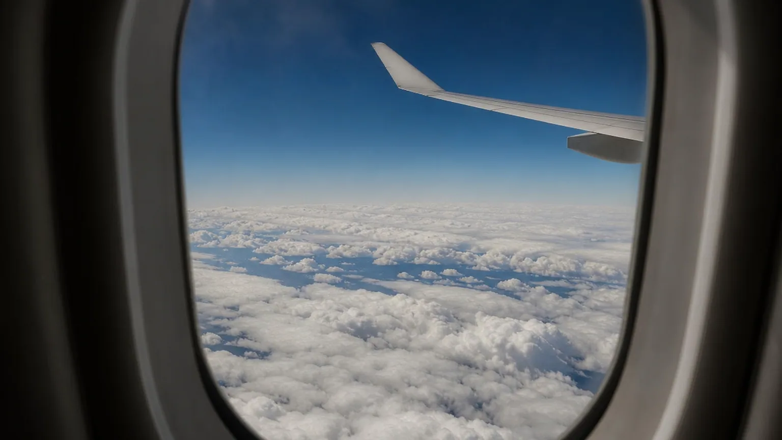 Avion de ligne vu depuis le hublot volant au-dessus d'une mer de nuages, ciel bleu profond, lumière de haute altitude.
