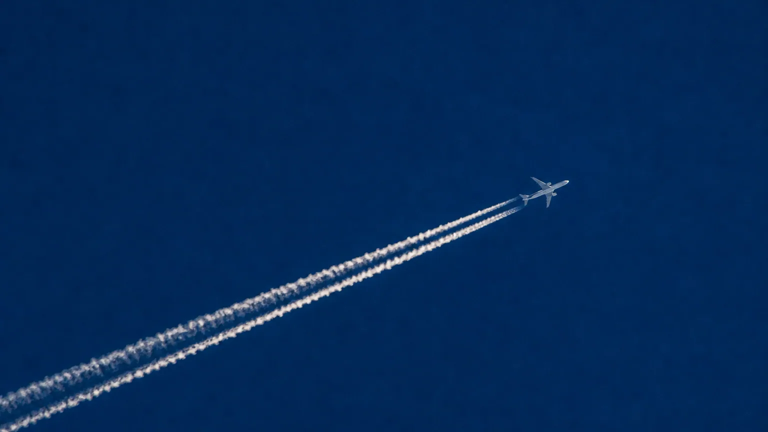 Un avion de ligne haut dans un ciel bleu, laissant derrière lui une longue traînée blanche rectiligne.