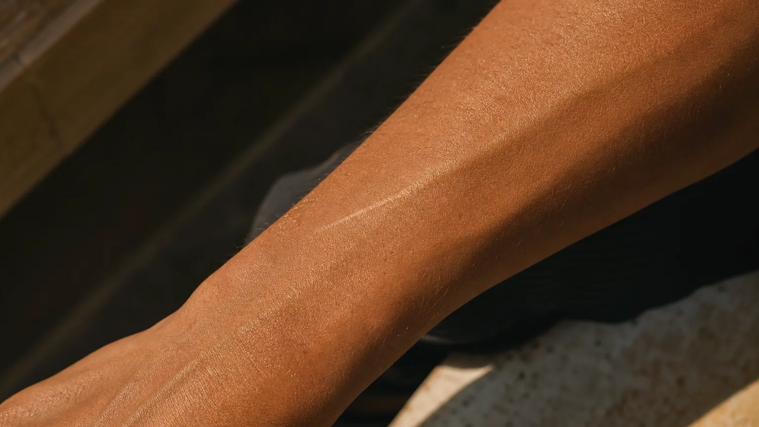 Gros plan sur une peau bronzée avec une fine cicatrice claire visible sur l'avant-bras, lumière naturelle d'été.