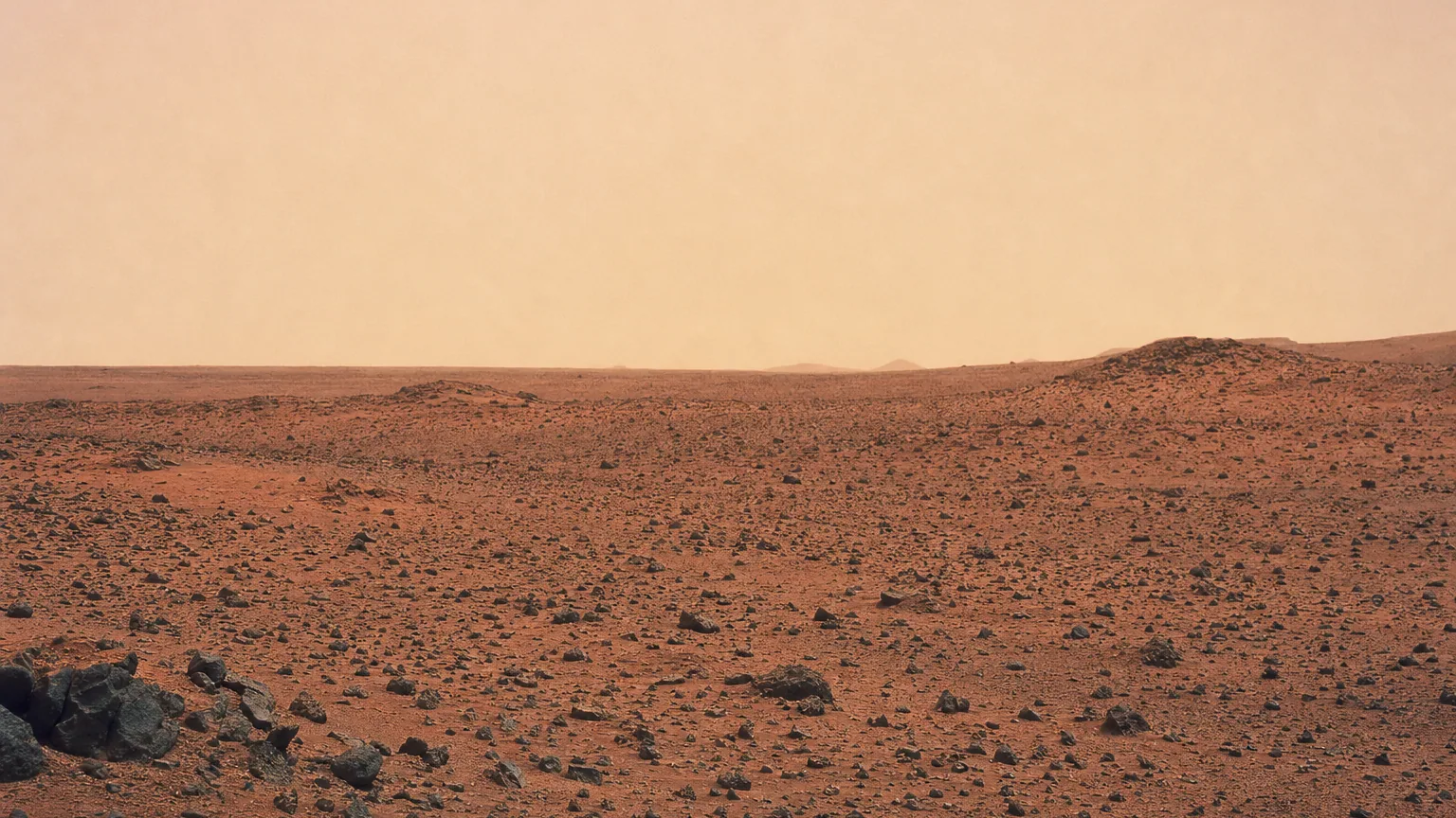 Plaine désertique ocre de Mars sous un ciel beige rosé voilé par la poussière en suspension.