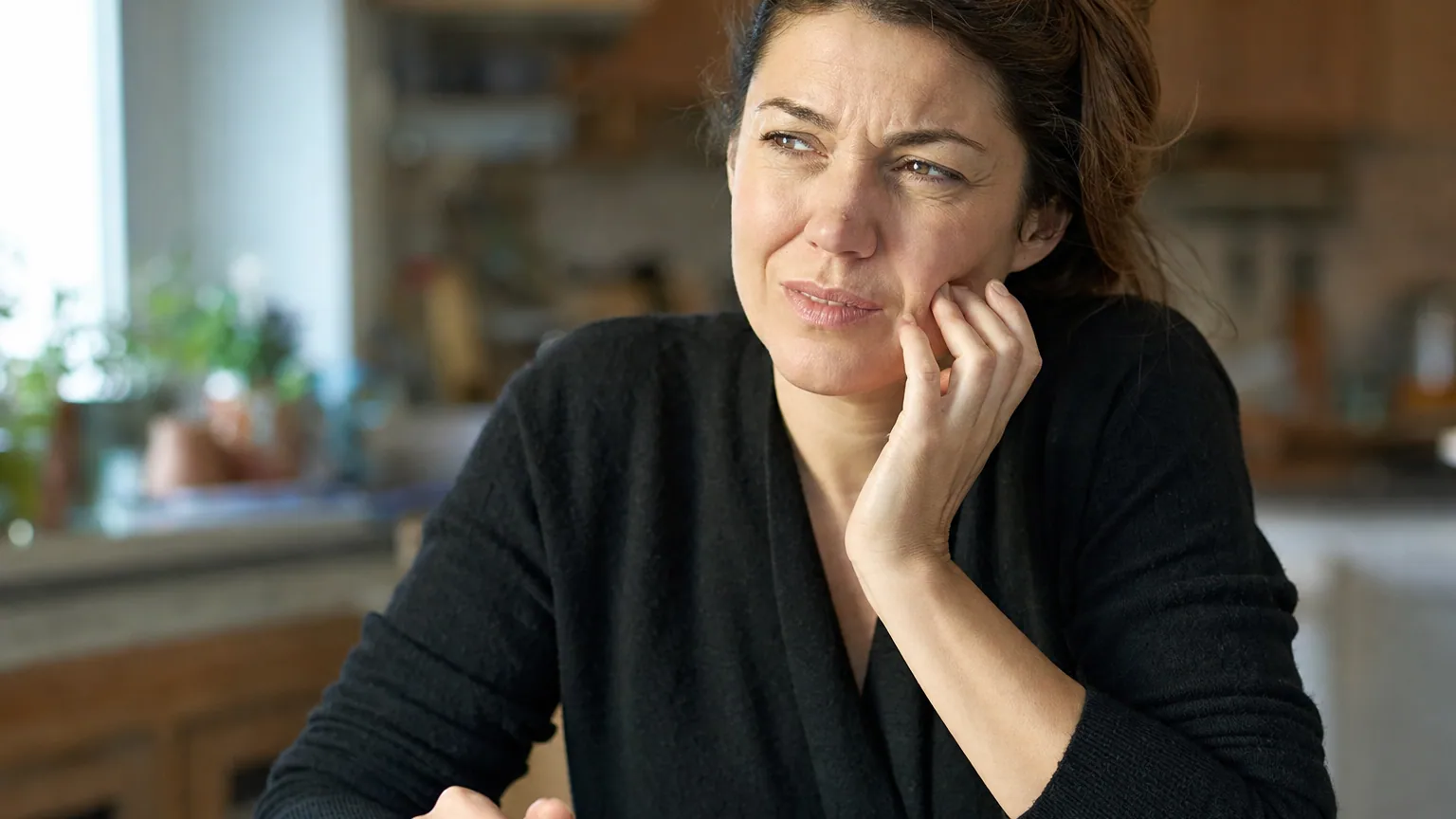 Une femme attablée dans sa cuisine éprouve une gêne en buvant son café, la main posée près de la bouche.