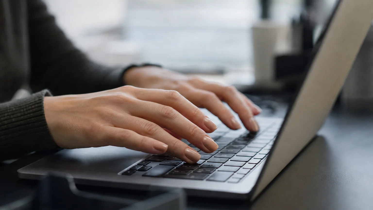 Gros plan de mains posées sur un clavier, ongles bien visibles, lumière naturelle douce de bureau.