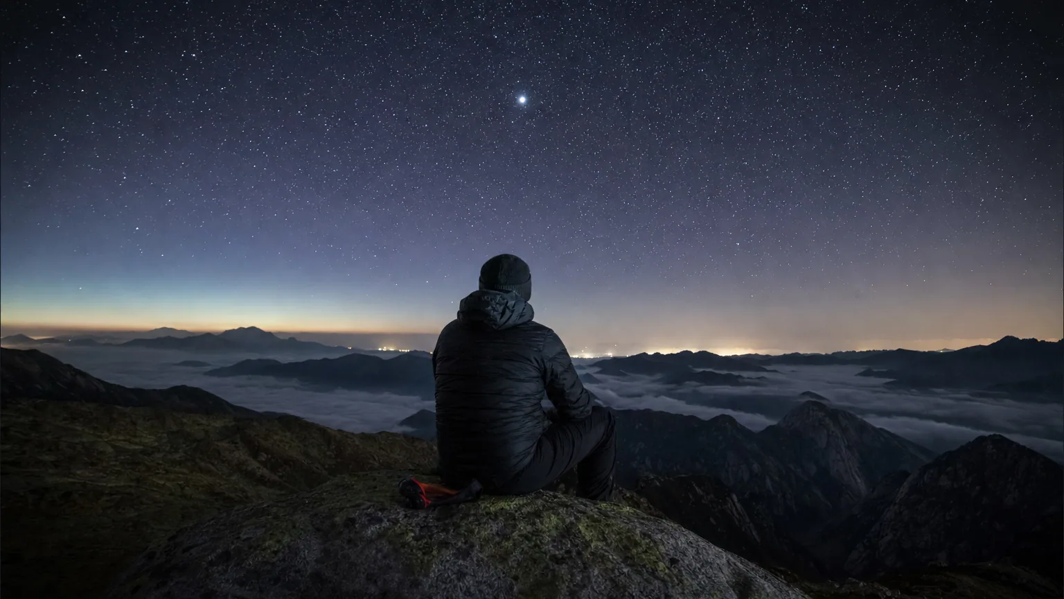 Un observateur de dos contemple un ciel étoilé en montagne, avec un astre plus brillant et stable au-dessus de l'horizon.