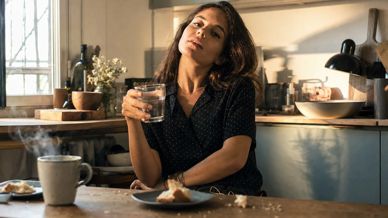 Une femme dans sa cuisine boit un grand verre d'eau d'un trait pour tenter de faire passer son hoquet.