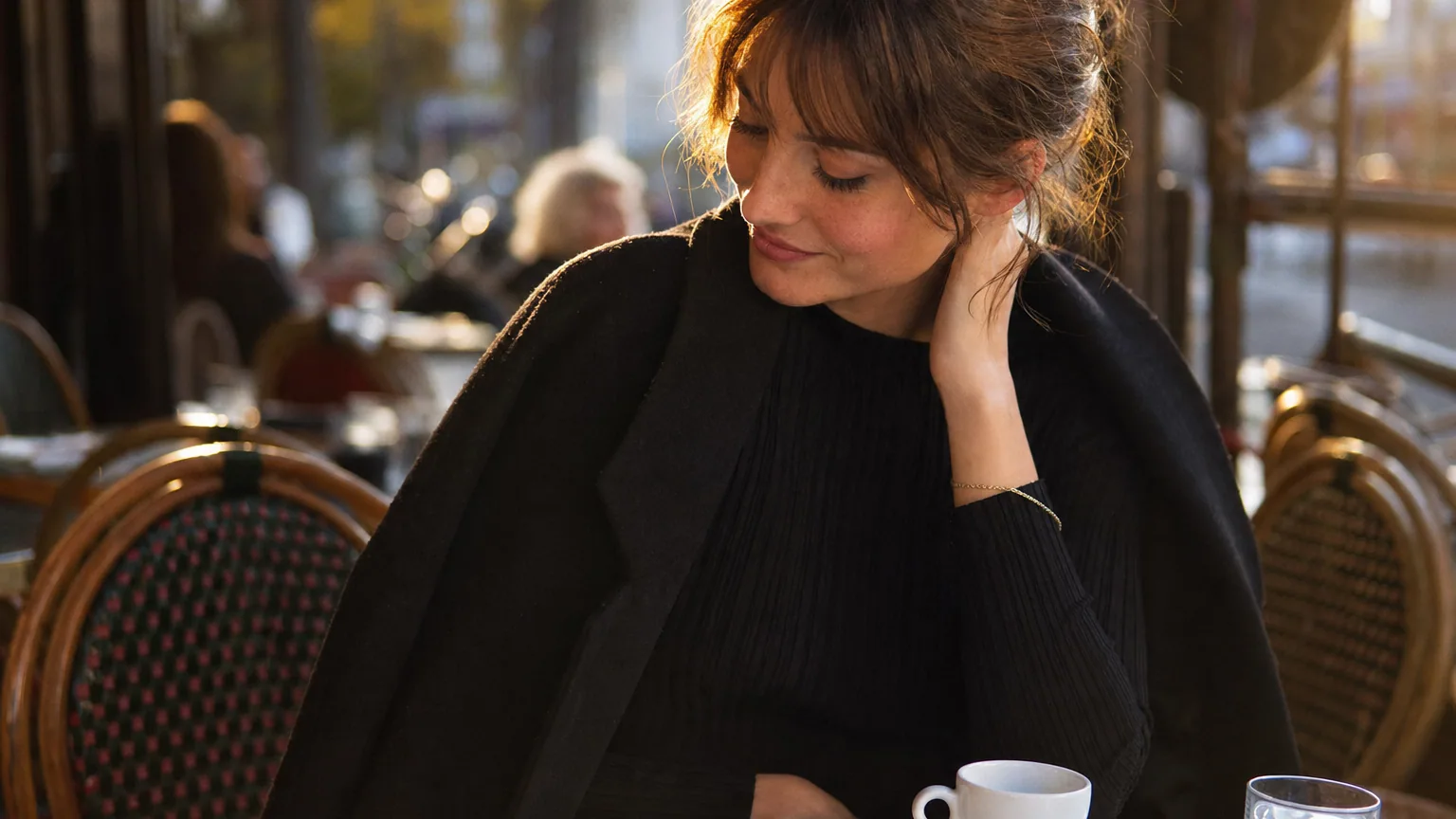 Jeune femme aux joues rougies baissant les yeux à la terrasse d'un café en fin d'après-midi