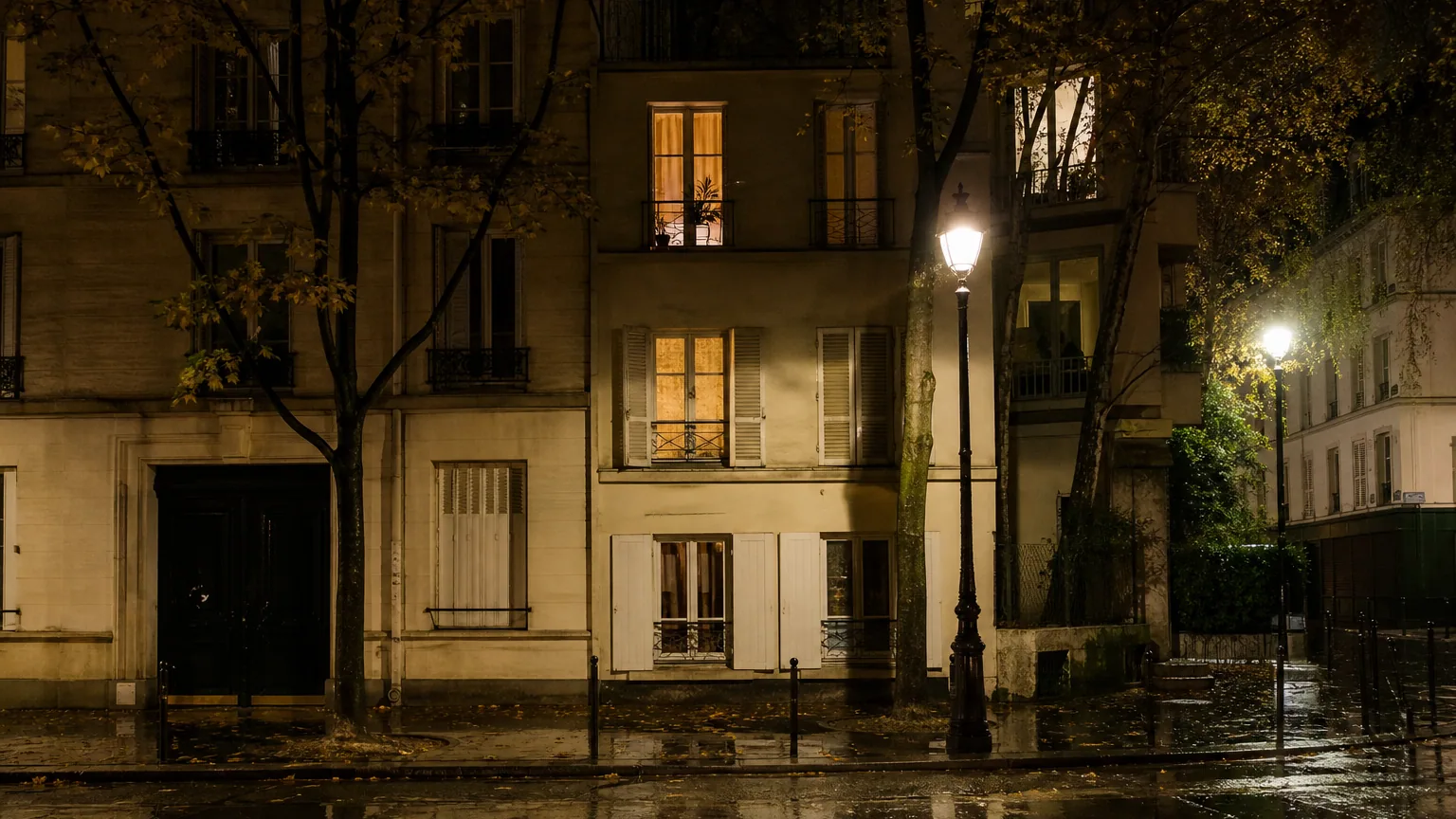 Fenêtres éclairées d'un immeuble résidentiel un soir d'automne pluvieux, vues depuis la rue mouillée éclairée par un lampadaire.